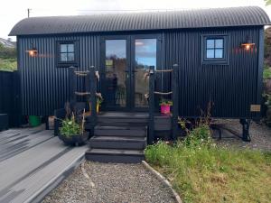 ein schwarzes kleines Haus mit einer Treppe, die zur Tür führt in der Unterkunft Delightful Shepherds Hut in Westport