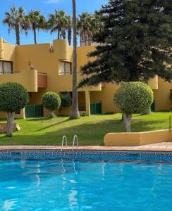 a swimming pool in front of a building with palm trees at Corralejo Garden House in La Oliva