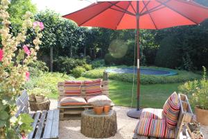 un patio con 2 sillas y una sombrilla roja en Authentieke privé-kamer bij Karen en Beveren