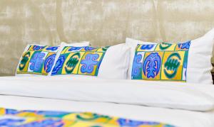 ロメにあるHotel M'Rodeのベッド(白いシーツ、カラフルな枕付)
