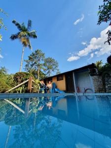 a swimming pool with a house and a palm tree at Pousada Donna Rose in Penedo