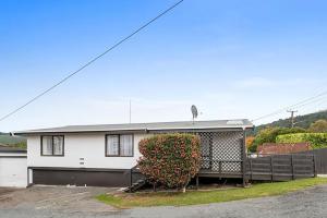 a white house with a fence and a bush at Comfortable Cosy Retreat in Rotorua
