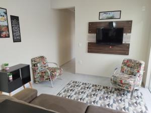 ein Wohnzimmer mit einem Sofa und Stühlen sowie einem Flachbild-TV in der Unterkunft Apartamento com garagem e perto das praias. in Palhoça