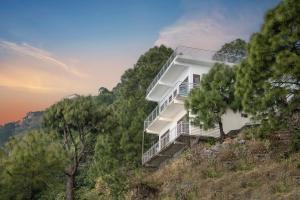 a white house on a hill with trees at Aravindam House I Open Rooftop & Garden I Bonfire I By Vanasthali Kasauli in Kasauli