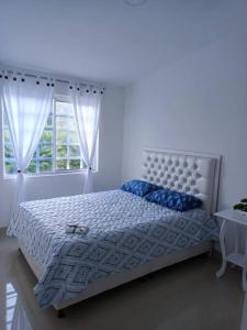 a white bedroom with a bed with blue pillows and a window at Apartamento Roldanillo pueblo mágico in Roldanillo