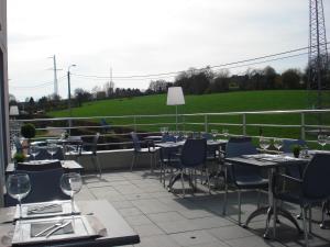 a patio with tables and chairs and a green field at Hotel Le Midi in Petit-Rechain