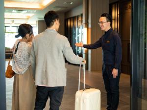 Grandvrio Hotel Beppuwan Wakura - ROUTE INN HOTELS - في بيبو: رجل وامرأة يتكلمان مع رجل معه حقيبة