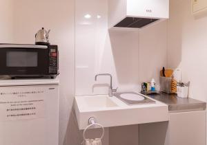 a white kitchen with a microwave and a sink at COCOSHUKU Nakano in Tokyo