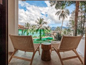 two chairs and a table on a balcony with palm trees at Resolution Resort in Ko Chang