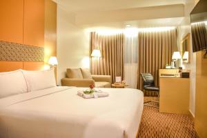 una habitación de hotel con una gran cama blanca y una silla en All Sedayu Hotel Kelapa Gading, en Yakarta