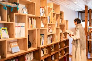 uma mulher numa biblioteca a olhar para um livro em 深々 books&stay シンシンブックスアンドステイ em Matsukawa