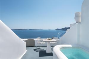 a white balcony with a table and a swimming pool at La Perla Villas and Suites - Adults Only in Oia