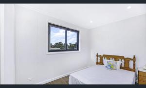 een witte kamer met 2 bedden en een raam bij New Gymea House in Gymea