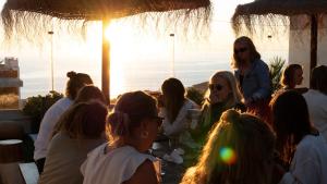 un grupo de personas sentadas alrededor de una mesa con la puesta de sol en The Salty Pelican Yoga & Surf Retreat, en Ericeira