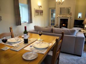 a dining room table with wine glasses and a couch at Cosy Stone Cottage, The Bungalow Perrotts Brook in Cirencester