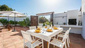 una mesa de comedor con sillas blancas y una sombrilla en el patio en Marrucho Alto Riogordo by Ruralidays, en Ríogordo