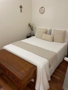 a large bed with white sheets and a clock on the wall at Apartamento Mimi in Figueira da Foz
