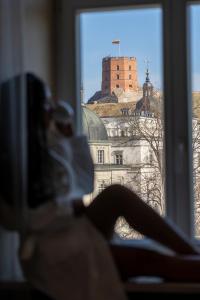 une femme assise sur un rebord de fenêtre donnant sur un château dans l'établissement Grand Hotel Vilnius, Curio Collection by Hilton, à Vilnius