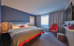 ケルンにあるHoliday Inn Express Cologne Mülheim, an IHG Hotelの大きなベッドと赤い椅子が備わるホテルルームです。