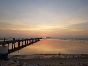 a pier on the beach with the sunset in the background at Jerai Geopark Cottage 3 bedrooms -Pulau Bunting in Yan