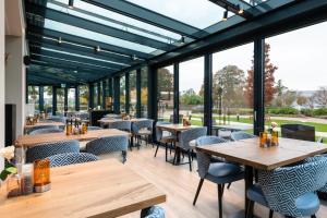 un ristorante con tavoli e sedie in legno e ampie finestre di Golden Tulip Ampt van Nijkerk a Nijkerk