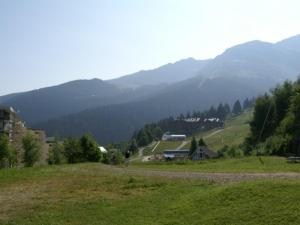 a green hill with a house and mountains in the background at Appartement Les Adrets-Prapoutel, 1 pièce, 3 personnes - FR-1-557-10 in Les Adrets