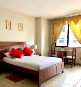 Un dormitorio con una cama con almohadas rojas y una mesa. en Hotel Onix Gold, en Guayaquil