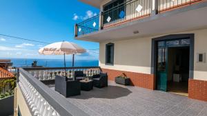 uma varanda com cadeiras e um guarda-sol e o oceano em Madeira Inn Refugio do Sol na Calheta