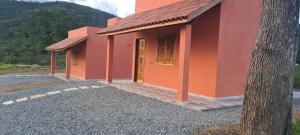 a small orange building with a tree in the foreground at Pousada Colina das Maritacas in São Thomé das Letras