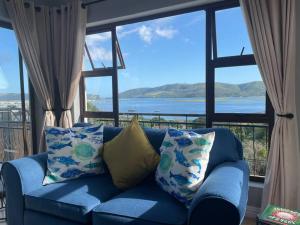 - un canapé bleu avec des oreillers devant une grande fenêtre dans l'établissement Solar-powered Lovely 1-Room Loft with amazing lagoon views!, à Knysna