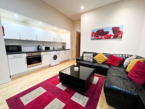 a living room with a black leather couch and a kitchen at Queen Street City Centre Apartment in Glasgow
