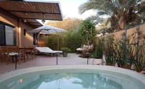 - une piscine dans un jardin avec une table et un parasol dans l'établissement אתיטיוד בערבה attitude at the arava, à H̱aẕeva