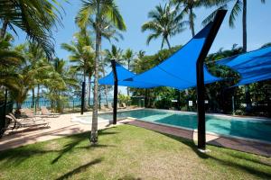 una piscina del complejo con sombrillas azules y palmeras en Ellis Beach Oceanfront Holiday Park, en Palm Cove