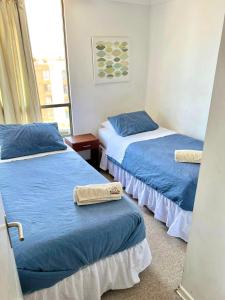 Habitación con 2 camas con sábanas azules y ventana en Apartamentos Alma Socoroma, en Arica