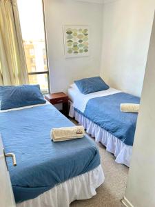 a room with two beds with blue sheets and a window at Apartamentos Alma Socoroma in Arica
