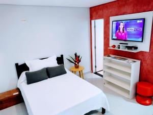 1 dormitorio con cama blanca y TV en la pared en Flat Ideal Guarujá - Apto Studio Mobiliado, Ar-Condic e Cozinha Completa, en Guarujá