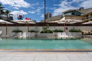 uma piscina com cadeiras brancas e guarda-sóis em Ruby Gold Coast By Serain em Gold Coast