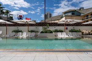 a swimming pool with white chairs and umbrellas at Ruby Gold Coast By Serain in Gold Coast