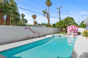 a swimming pool in front of a white wall with palm trees at La Vie en Rose Permit# 3901 in Palm Springs