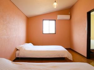 twee bedden in een kamer met oranje muren en een raam bij 瀬戸内隠れ家リゾート in Onomichi