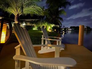 two white chairs sitting on a dock by the water at night at New! Waterfront Heated Pool & Jacuzzi 2 mi to Beach - Fishing Pier Relaxing SPA & Hammock in Fort Lauderdale