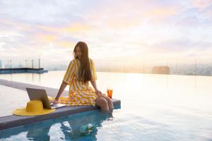 a woman sitting on the edge of a swimming pool with a laptop at Momentus Hotel Alexandra in Singapore