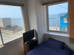Un dormitorio con una cama y un televisor y ventanas. en Zenibako House 3F-RoomC, en Otaru