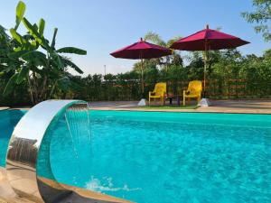 uma piscina com dois guarda-sóis e uma mesa e cadeiras em Lampang Hideaway Guesthouse em Lampang