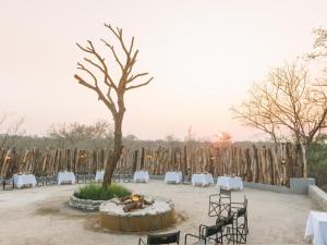 eine Feuerstelle mit Tischen, Stühlen und einem Baum in der Unterkunft The Orpen Kruger in Welverdiend