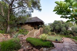 a garden with a house with a thatched roof at Olarro Lodge in Maji Moto