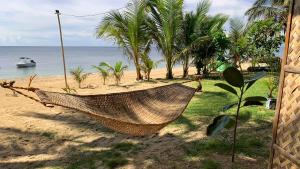 a hammock on a beach with a boat in the water at The Beach House Carabao Island in San Jose