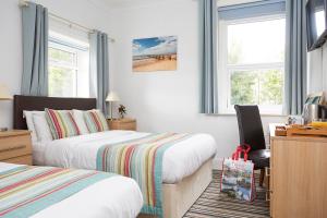 a bedroom with two beds and a desk and two windows at Luccombe Manor Country House Hotel in Shanklin