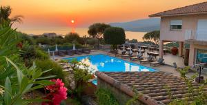 a pool with chairs and a sunset in the background at Résidence & Hôtel Aria Marina in Propriano