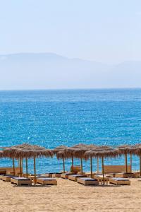 a row of straw umbrellas and chairs on a beach at Dionysos Seaside Resort Ios in Mylopotas